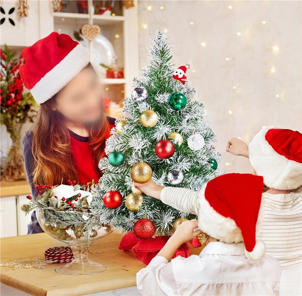 Kinder dekorieren einen kleinen, mit farbigen Kugeln geschmückten Weihnachtsbaum.