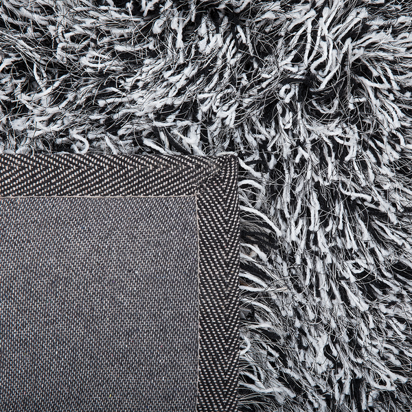 Hochflor-Teppich in Nahaufnahme mit schwarz-weißen Fasern und gewebter Rückseite mit Fischgrätenmuster.