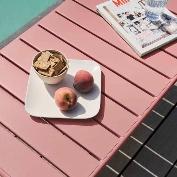 Gartentisch aus Metall mit Lamellen, auf dem ein Teller mit Pfirsichen, Keksen, eine Zeitschrift und ein Glas Wasser stehen.