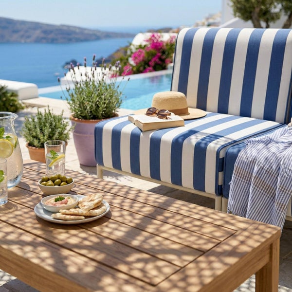Gestreiftes Lounge-Sofa in Blau und Weiß auf einer hellen Terrasse mit Holztisch, Pool und Blick auf das Meer.