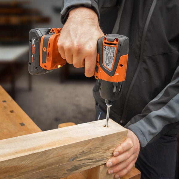 Eine Person schraubt mit einem Akku-Schlagschrauber eine Schraube in ein Holzstück.