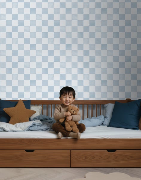 Helles Kinderzimmer mit einem Holzbett inklusive Schubladen und einer hellblau-weiß karierten Tapete an der Wand.