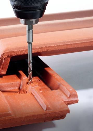 Eine Bohrmaschine bohrt in einen Dachziegel.