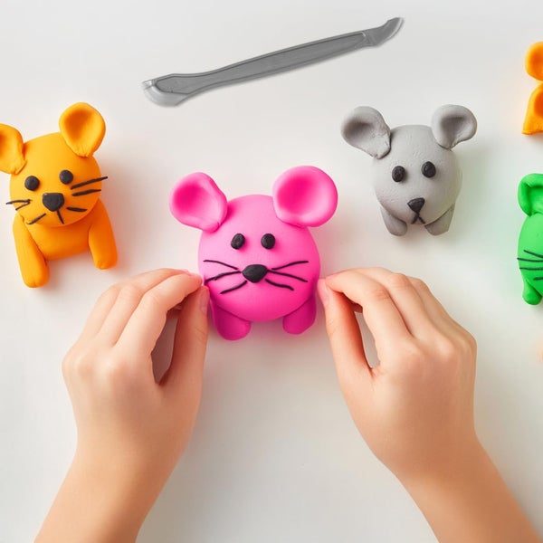 Hände formen kleine Mäusefiguren aus bunter Knete, Modellierwerkzeug im Hintergrund.