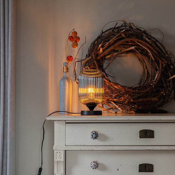 Dekorative Tischleuchte auf einer Kommode mit Kranz und Flasche