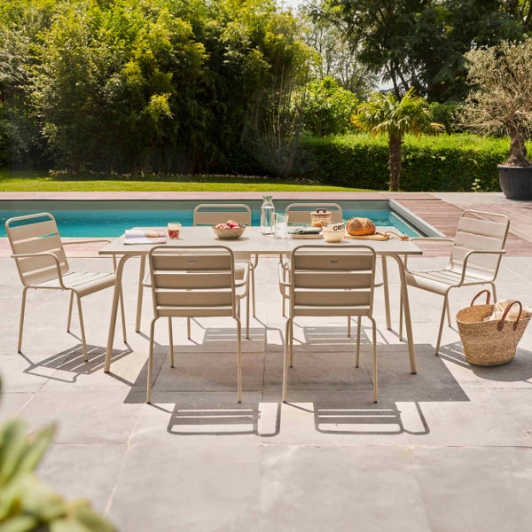 Moderne Garten-Essgruppe aus beigem Metall mit Tisch und sechs Stühlen auf einer sonnigen Steinterrasse am Pool im Garten.