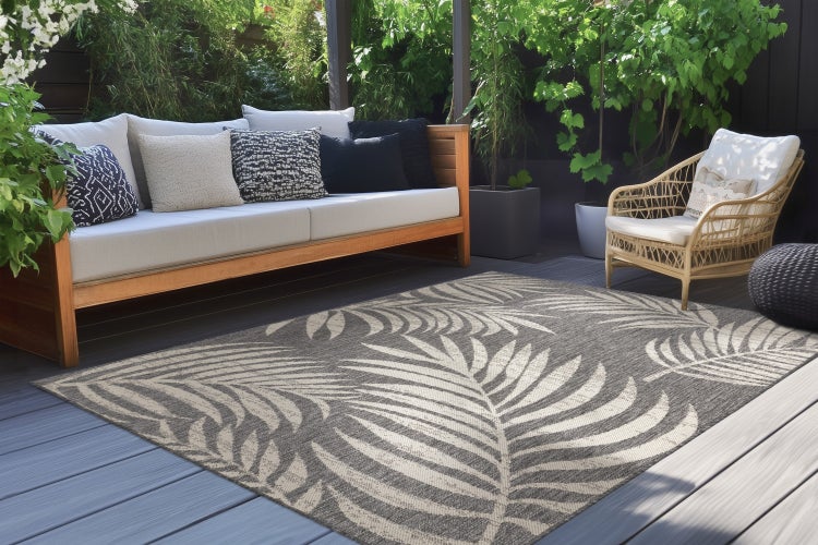 Outdoor-Teppich mit Blättermuster auf einer Holzterrasse mit gemütlicher Lounge-Ecke und Pflanzen.