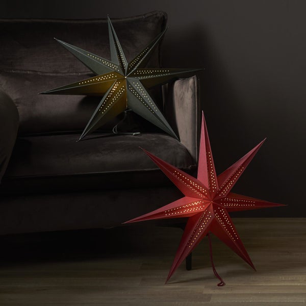Zwei beleuchtete Papiersterne in unterschiedlichen Größen stehen vor einem Sofa.