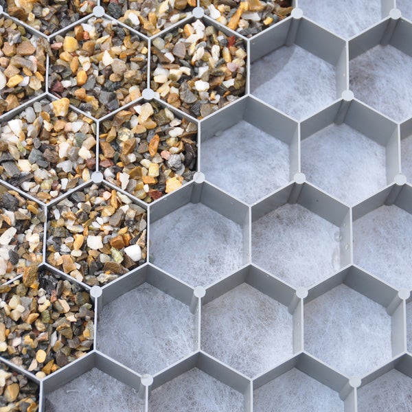 Kieswabenmatte aus Kunststoff zur Bodenstabilisierung, teilweise mit Zierkies befüllt auf einer Unterlage aus Vlies.