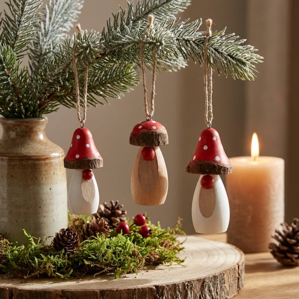 Drei hängende Holzpilz-Weihnachtsanhänger an einem Tannenzweig mit Moos, Zapfen und einer brennenden Kerze als weihnachtliche Dekoration