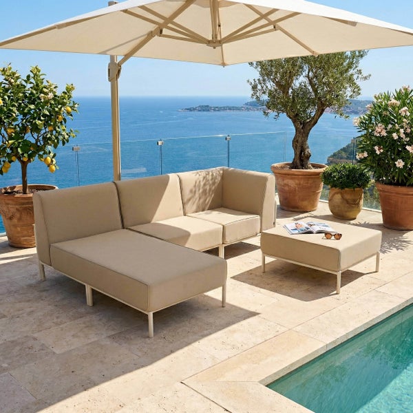 Modernes Gartenlounge-Set mit modularem Sofa und Hocker auf einer hellen Steinterrasse am Pool unter einem großen Sonnenschirm mit Meerblick.