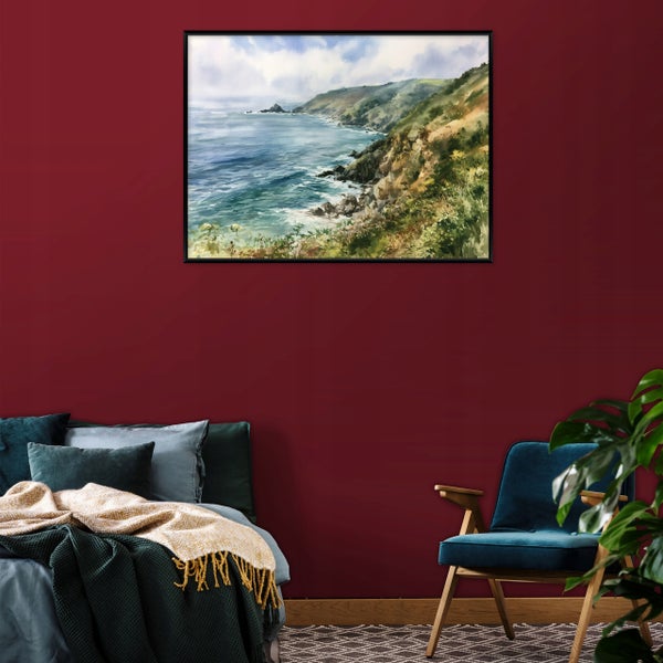 Wandbild mit Küstenlandschaft in schwarzem Rahmen über einem Bett mit Sesseln und Zimmerpflanze
