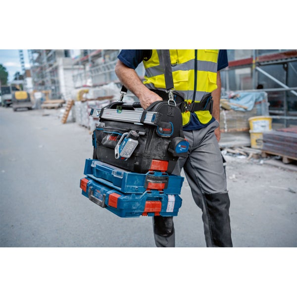 Eine Person auf einer Baustelle trägt eine Bosch Professional Werkzeugtasche mit zwei angekoppelten L-BOXXen.