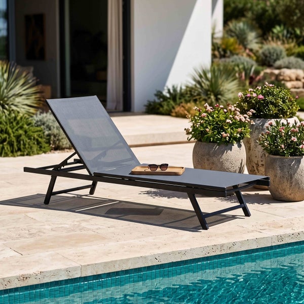 Moderne Gartenliege mit Metallgestell und Textilbespannung auf einer hellen Steinterrasse am Pool mit Pflanzgefäßen.