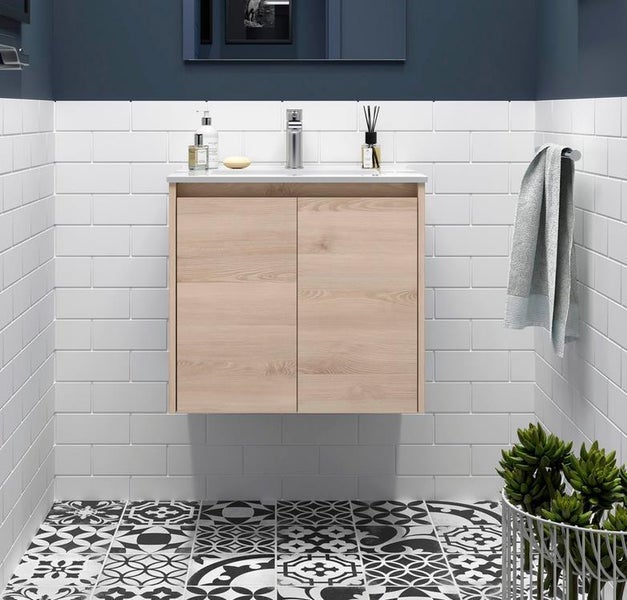 Hängender Waschtischunterschrank in heller Holzoptik mit weißem Waschbecken in einem Badezimmer mit weißen Metrofliesen und gemustertem Boden.