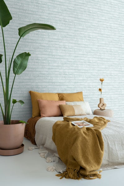 Dekoratives Schlafzimmer mit Bett, Kissen, Tagesdecke, Zimmerpflanze und gemusterter Tapete