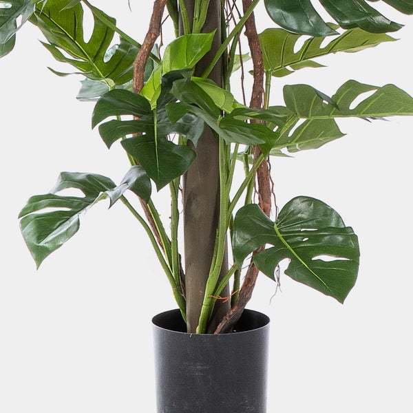 Künstliche Monstera-Pflanze mit grünen Blättern und Kletterhilfe in einem schwarzen Topf.