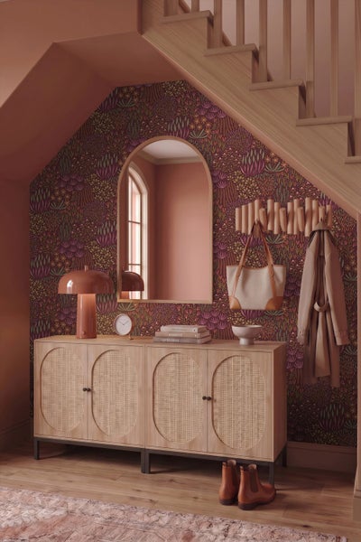 Moderner Flur mit Holzsideboard mit Rattantüren, floraler Tapete, einem Bogenspiegel und Holzgarderobe unter einer Treppe.