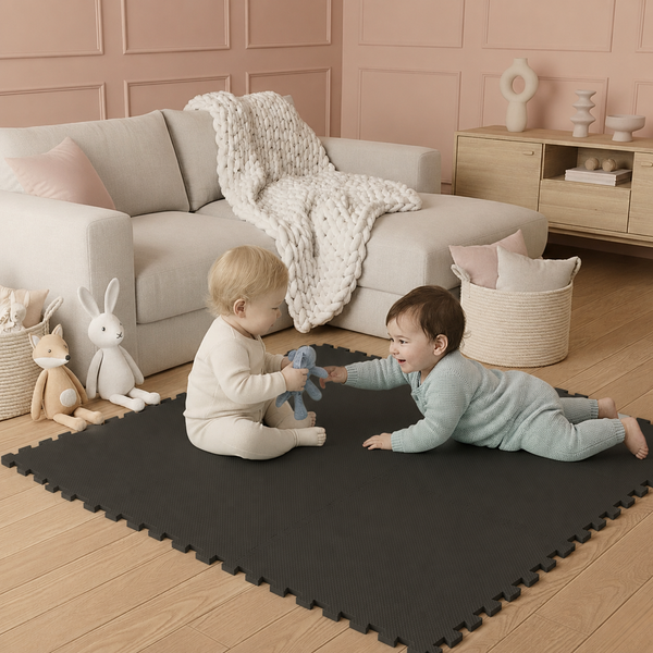 Zwei Kleinkinder spielen auf schwarzen Schaumstoff-Puzzlematten in einem hellen, organisierten Wohnzimmer mit Sofa und Holzmöbeln.