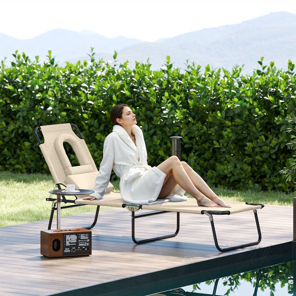 Beige Gartenliege mit Gesichtsausschnitt und Kissen auf einer hellen Holzterrasse am Pool, eine Frau im weißen Bademantel sitzt darauf.