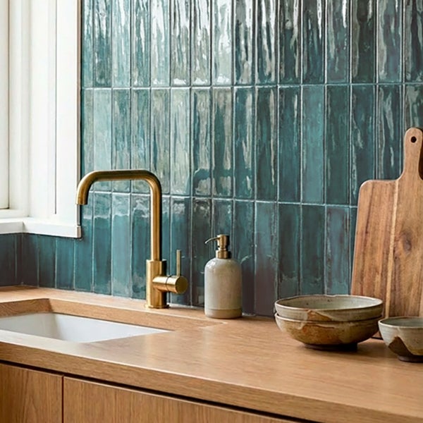 Moderne Kuechenzeile mit Wandfliesen im Hochformat ueber einer Arbeitsplatte aus Holz und einem Waschbecken mit Armatur in Metalloptik.
