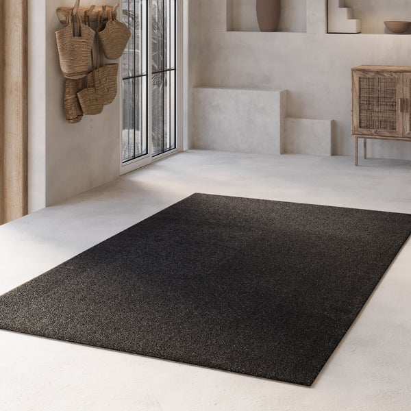 Moderner rechteckiger dunkler Teppich in einem hellen, minimalistischen Raum mit strukturierten Wänden, geflochtenen Körben und Holzschrank.