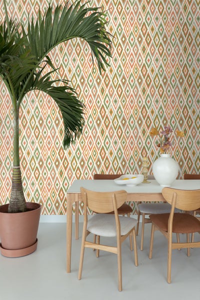 Esszimmer mit Esstisch, Stühlen und einer Wand mit Rautenmuster-Tapete sowie einer Topfpflanze