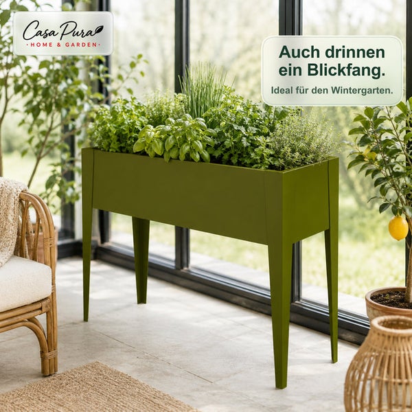 Hochbeet auf Beinen mit frischen Kräutern bepflanzt, in einem hellen Wintergarten neben einem großen Fenster und einem Rattan-Sessel.