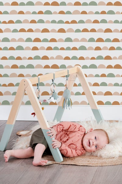 Baby liegt unter einem Spielbogen aus Holz mit Spielzeug