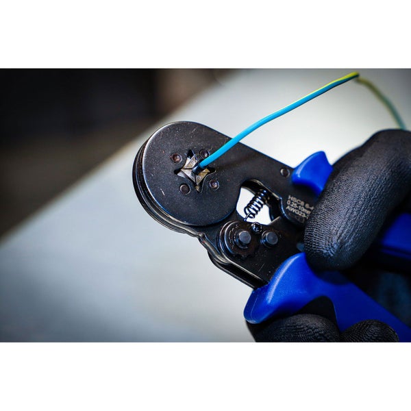 Eine Crimpzange mit einer blauen und gelben Aderendhülse, gehalten von einer Hand mit Handschuh