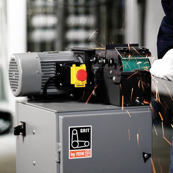 Bandschleifmaschine im Einsatz mit Funkenflug. GRIT by FEIN Logo sichtbar. Eine Person mit Schutzhandschuhen schleift ein Werkstück am Schleifband.