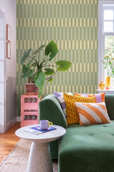 Helles Wohnzimmer mit geometrisch gemusterter Tapete, Samtsofa mit Zierkissen, Beistelltisch und einer großen Zimmerpflanze.