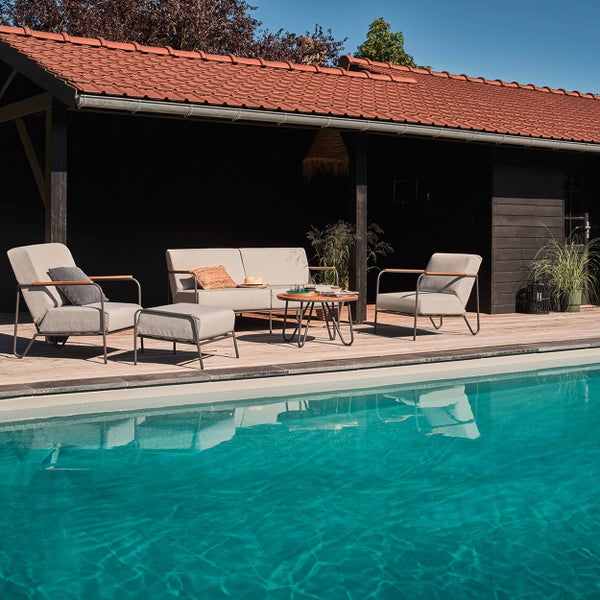 Moderne Gartenlounge-Garnitur bestehend aus Sofa, zwei Sesseln, Hocker und rundem Holztisch auf einer Holzterrasse neben einem Pool.