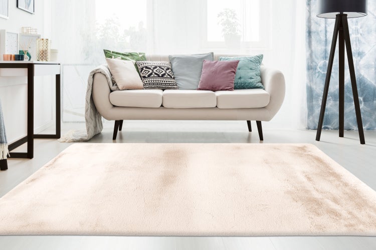 Ein rechteckiger, flauschiger Wohnzimmerteppich mit kurzem Flor in einem hellen, neutralen Ton, platziert vor einem Sofa im Wohnzimmer.