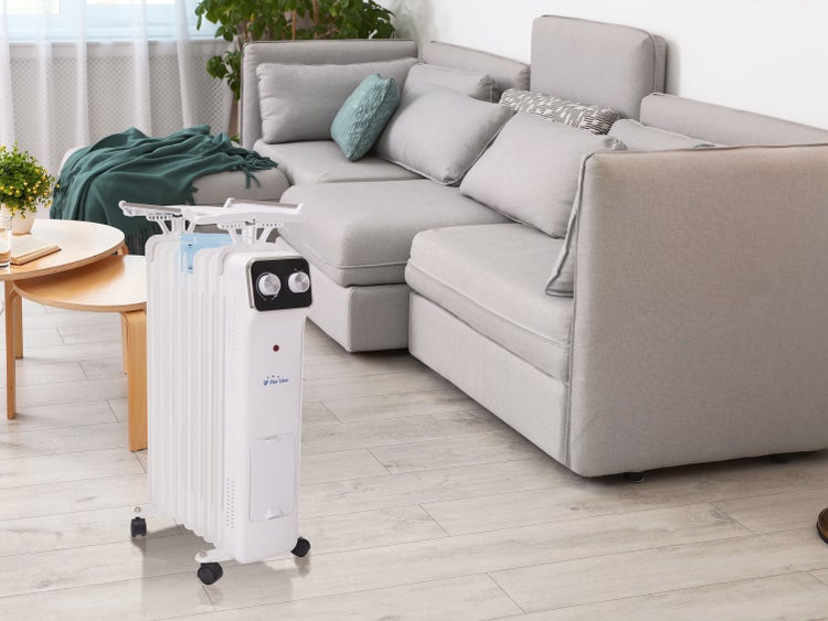 Weißer Ölradiator von Pur Line mit Wäscheständerfunktion in einem hellen Wohnzimmer neben einem grauen Sofa.