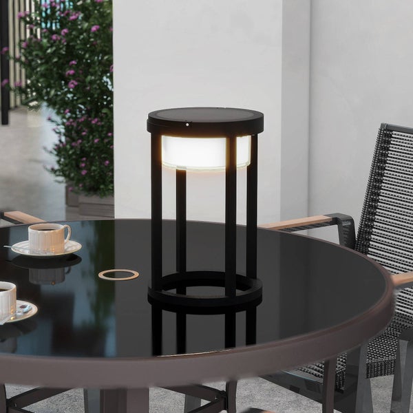 Moderne LED-Außen-Tischleuchte mit schwarzem Metallgestell auf einem dunklen Terrassentisch neben einer Kaffeetasse und Flechtstuhl.