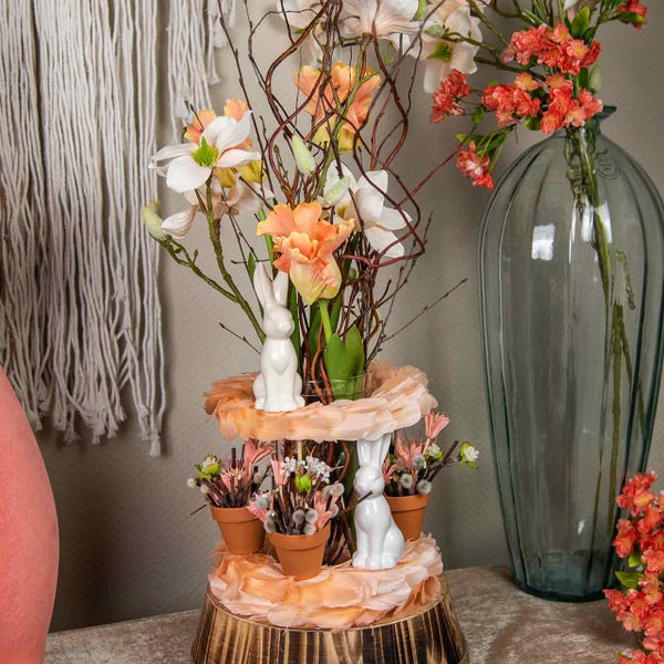Dekoration mit Blumen, Ästen, Blumentöpfen und Hasenfiguren auf einem dreistufigen Holzständer