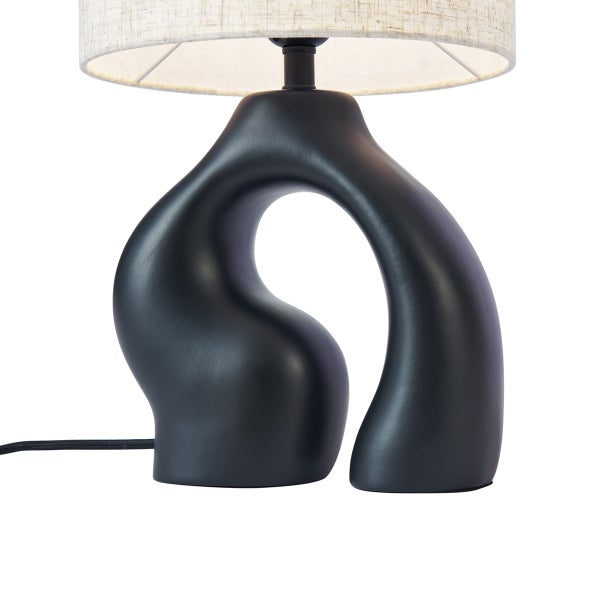 Moderne Tischleuchte mit organisch geformtem mattschwarzem Fuß und hellem Stoffschirm aus Leinen.