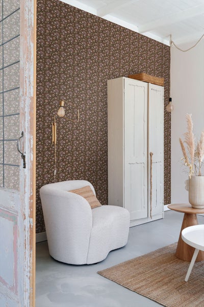 Wohnzimmer mit gemusterter Tapete, Sessel, Schrank und Teppich