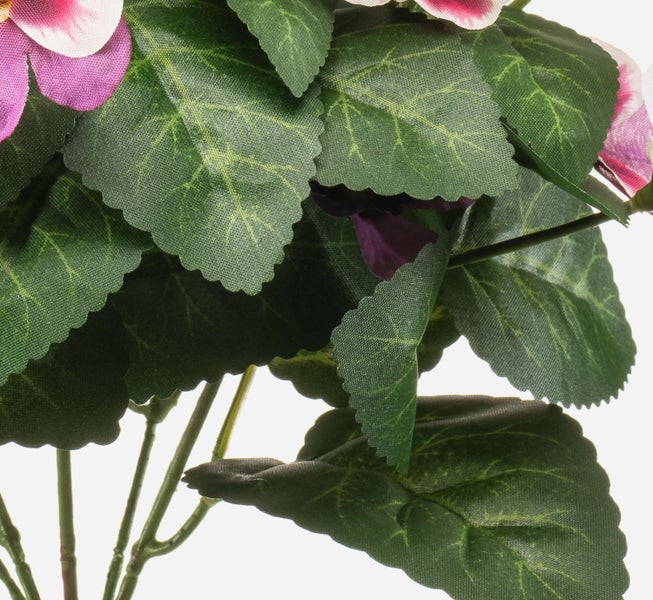 Nahaufnahme einer Kunstpflanze mit grünen gezackten Blättern und violetten Blütenblättern.