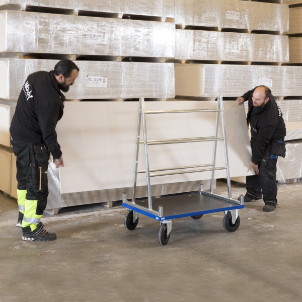 Zwei Arbeiter transportieren Gipskartonplatten mit einem Transportwagen in einem Lager.
