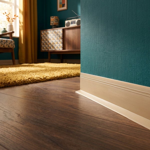 Fußleiste in Holzoptik angebracht an einer Wand mit Struktur-Tapete im Übergang zu einem Laminatboden in einem Wohnzimmer.