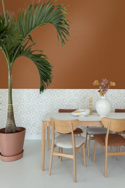Moderner Essbereich mit Holztisch und Stühlen, eine große Topfpalme links, zweigeteilte Wand mit Wandfarbe und hellem geometrischem Muster.