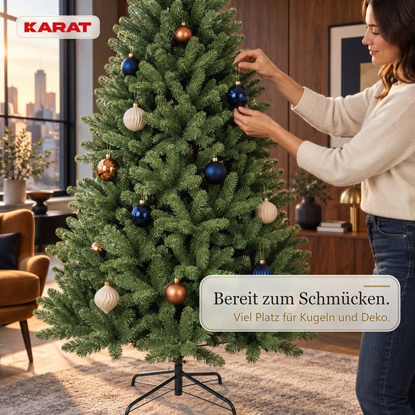 Eine Frau schmückt einen künstlichen Weihnachtsbaum mit Weihnachtskugeln im Wohnzimmer. Karat Logo.