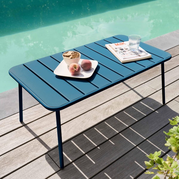 Blauer rechteckiger Outdoor-Couchtisch aus Metall auf einer Holzterrasse am Pool mit Obst und einer Zeitschrift.