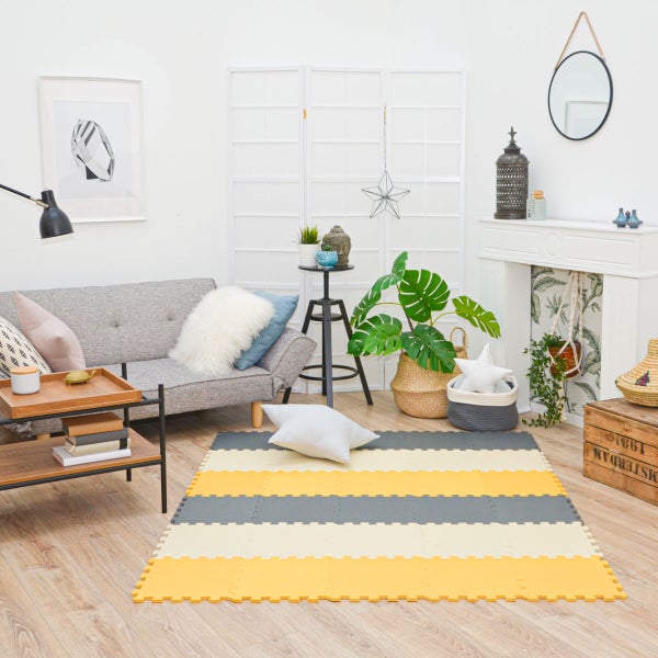 Hell eingerichtetes Wohnzimmer mit grauem Sofa, Holzfußboden und einer gestreiften Puzzlematte. Enthält Pflanzen, einen weißen Kaminumbau und Paravent.