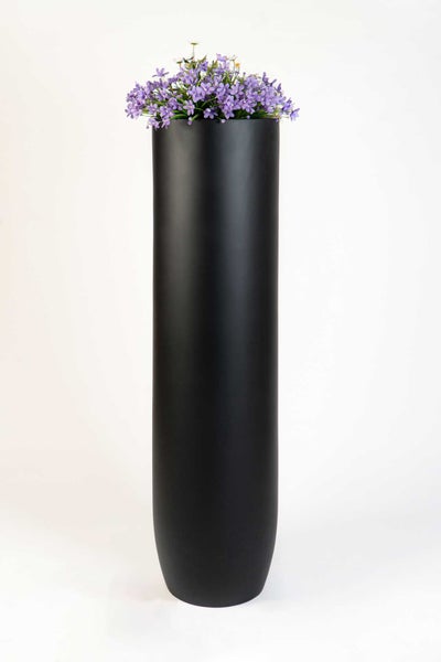 Hohes zylindrisches Pflanzgefäß in Schwarz mit lila Blumen.