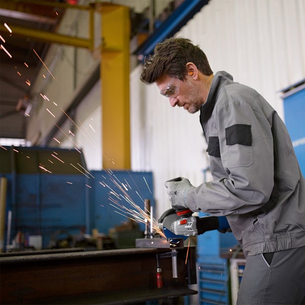 Ein Arbeiter in Arbeitskleidung verwendet einen Winkelschleifer mit Funkenflug zum Schleifen von Metall.