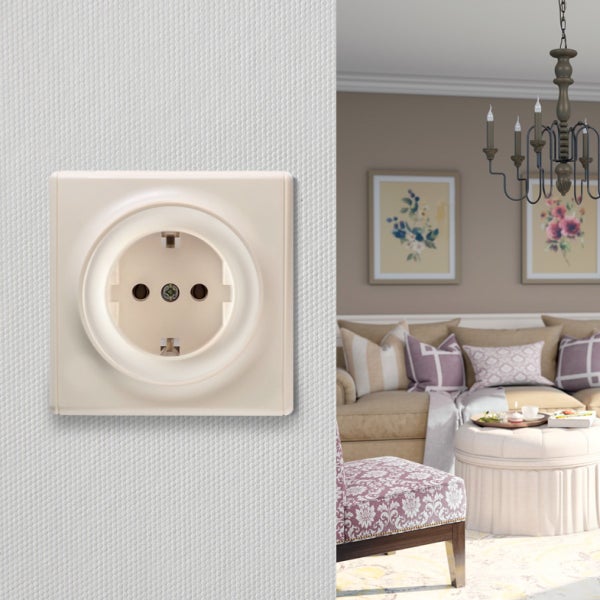 Steckdose in klassischem Design auf einer strukturierten Wand, im Hintergrund ein gemütlich eingerichtetes Wohnzimmer mit Kronleuchter.