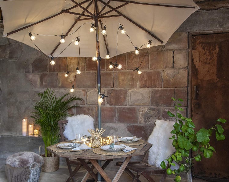 Dekorierter Gartentisch mit Sonnenschirm und Lichterkette für eine stimmungsvolle Atmosphäre im Garten.